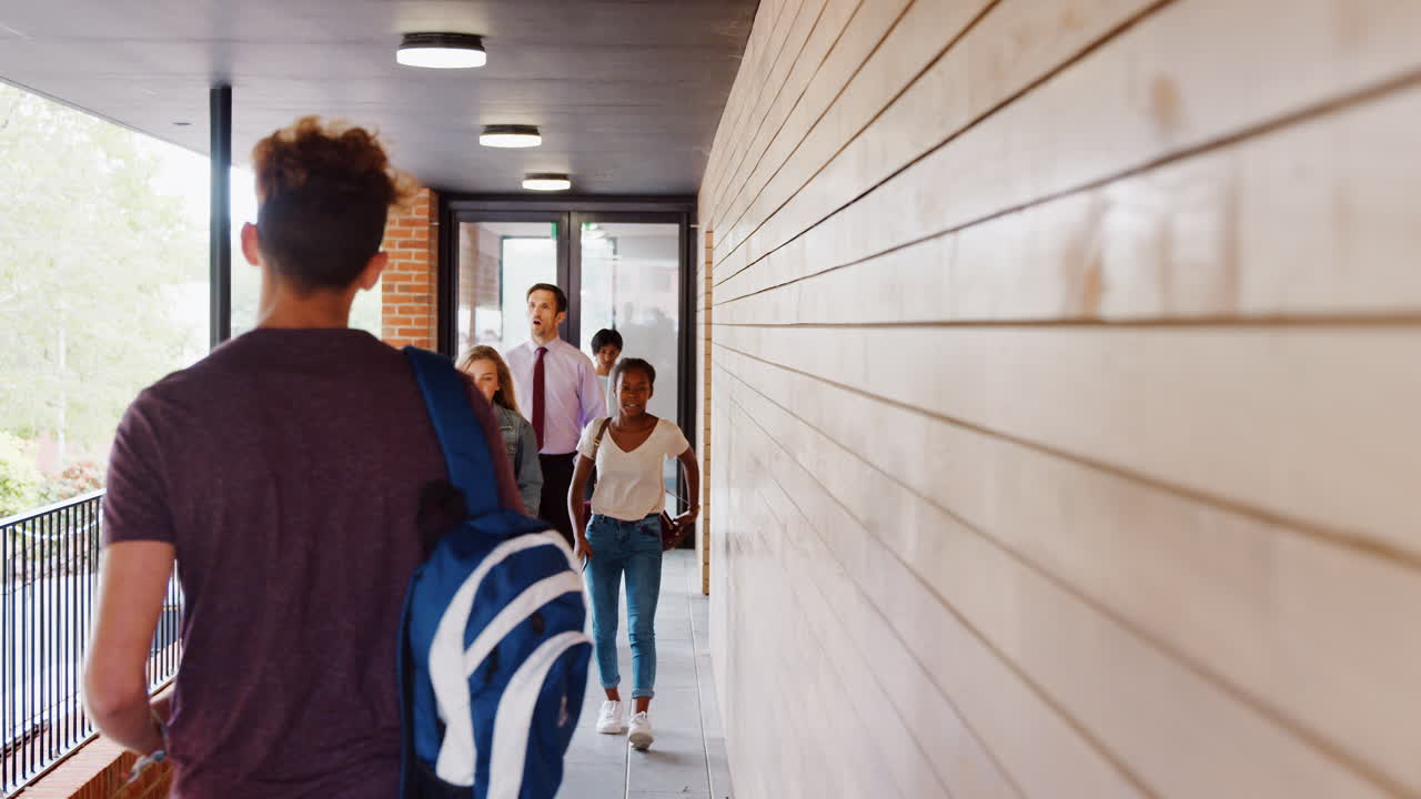 십대 학생과 교사가 학교 건물 사이를 고 있습니다.