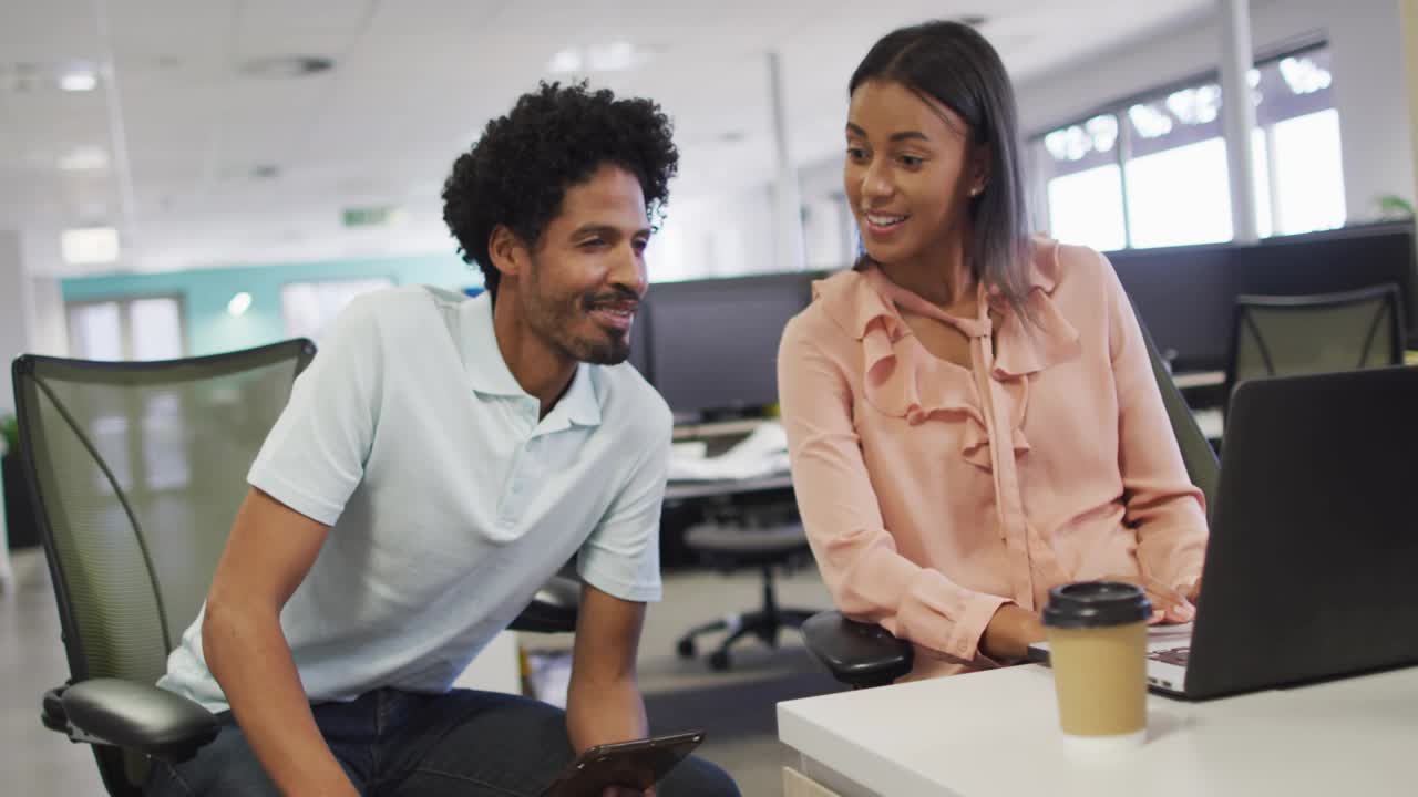 Two coworkers sitting desk, woman typing while man pointing, social icons rising, tracking metrics