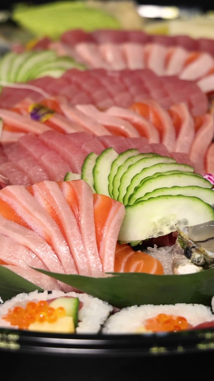 Un'inquadratura verticale dettagliata di salmone, tonno, ostriche e maki che ruotano su un piatto da portata.