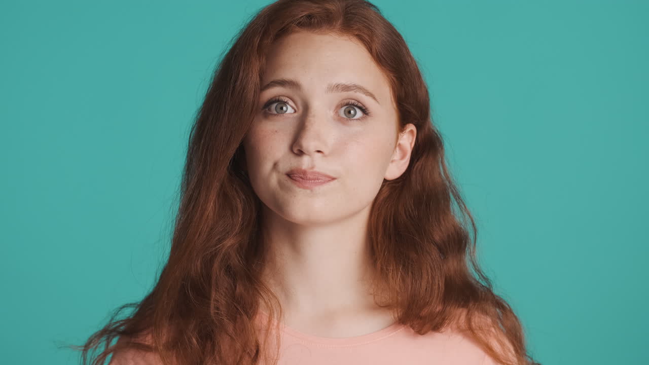 рыжая девушка перед камерой на бирюзовом фоне.