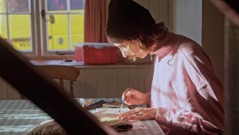 artist paints a water colour painting in a cottage, painter at work, side profile, mid shot, creativity