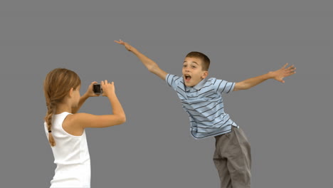 sister taking pictures of her brother jumping on grey screen