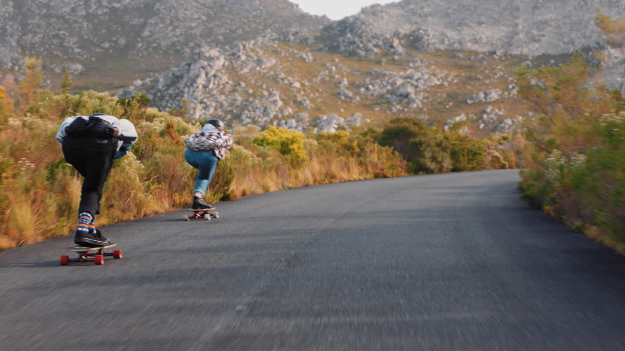 jóvenes amigos haciendo longboard juntos disfrutando de carreras competitivas navegando rápido cuesta abajo divirtiéndose montando en patineta usando casco protector vacaciones de verano deporte vista trasera