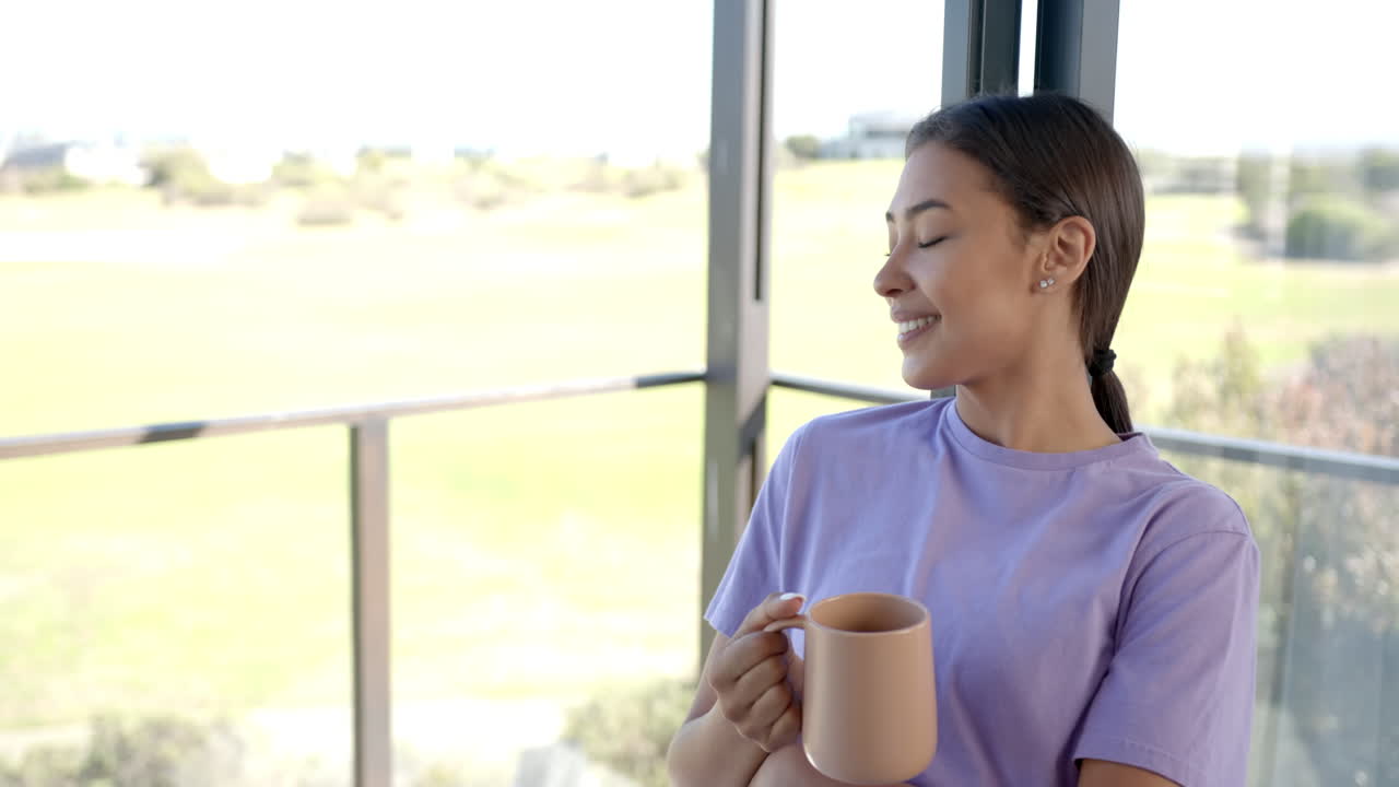 Enjoying morning coffee, woman in purple shirt relaxing by window at home, copy space