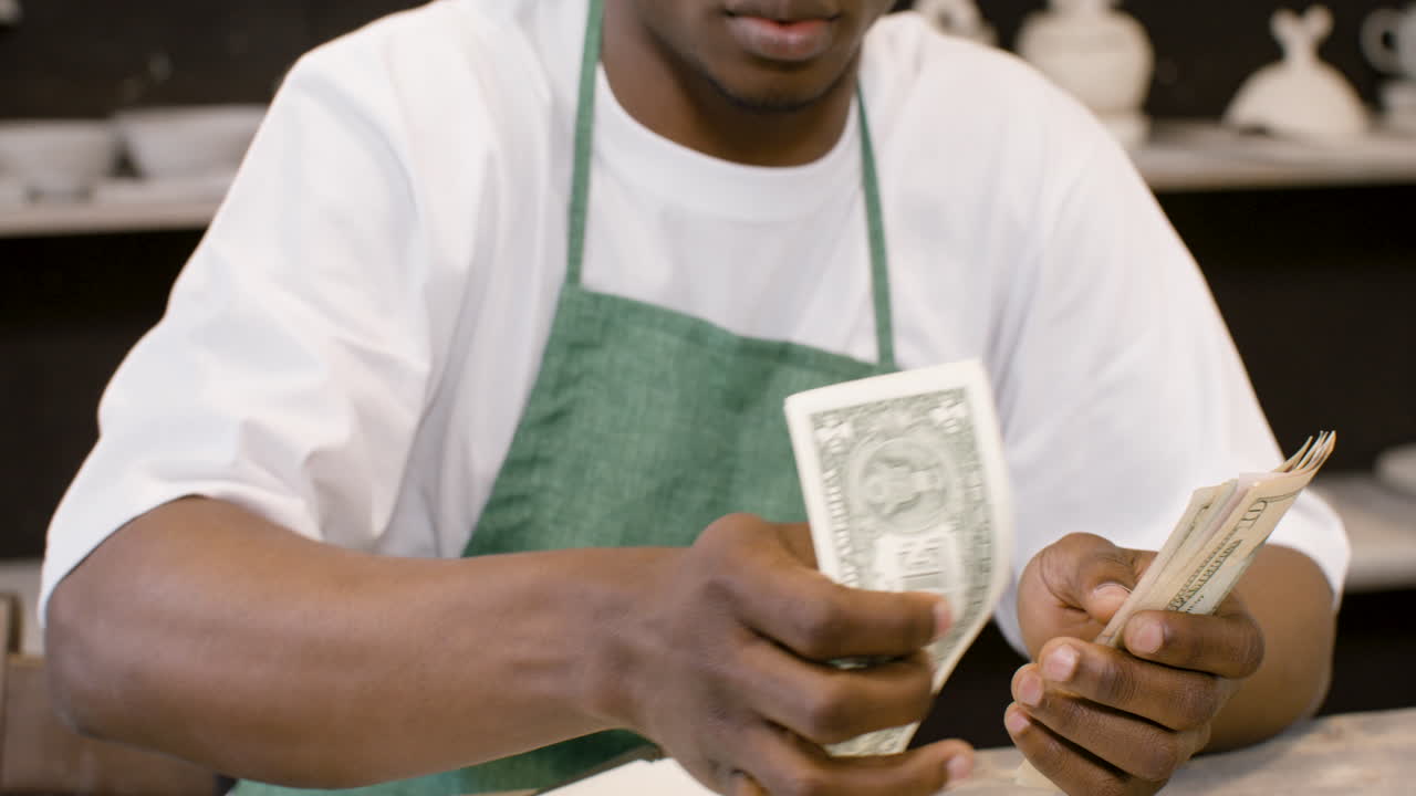 Male Small Business Owner Counting Money In The Pottery Shop