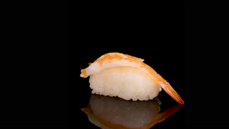 shrimp sushi rotates smoothly on a reflective black surface, illuminated by soft studio lighting. camera remains stationary, emphasizing the sushi’s texture and detail