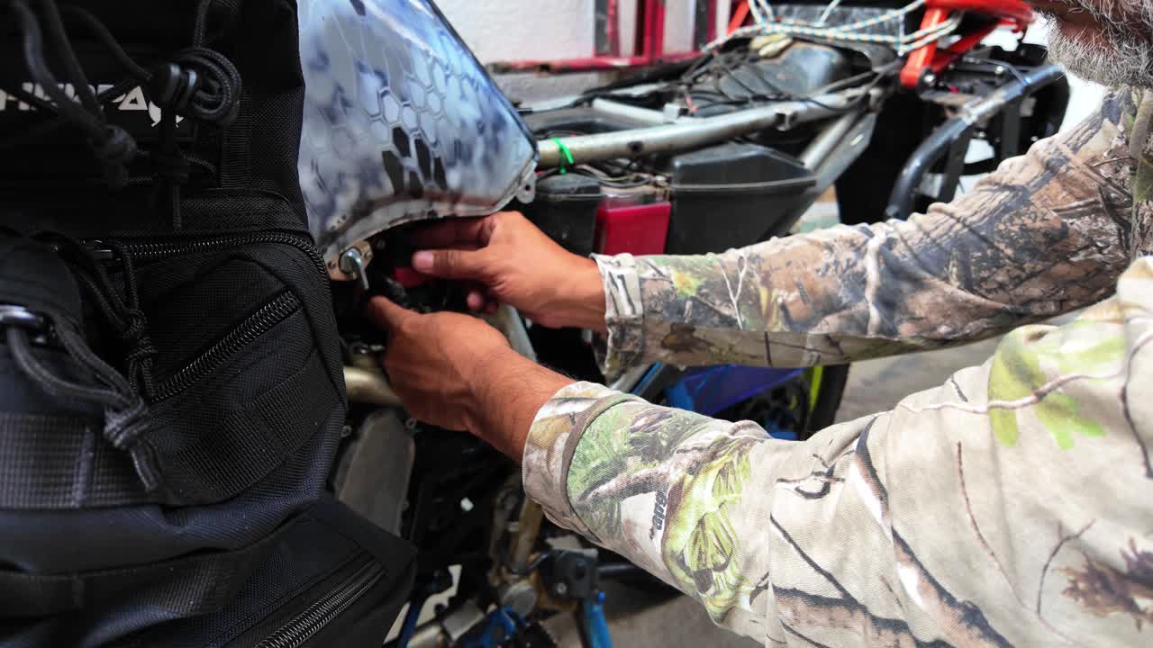 Close-up of adult man working on motorcycle, replacing a small fuse in electrical system. Hands and tools in action while performing mechanical maintenance outdoors