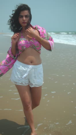 confident young woman in pink beachwear walking along the shoreline on a sunny day