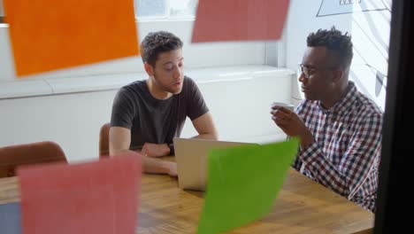 Front-view-of-young-mixed-race-business-team-drinking-coffee-and-working-on-laptop-in-office-4k