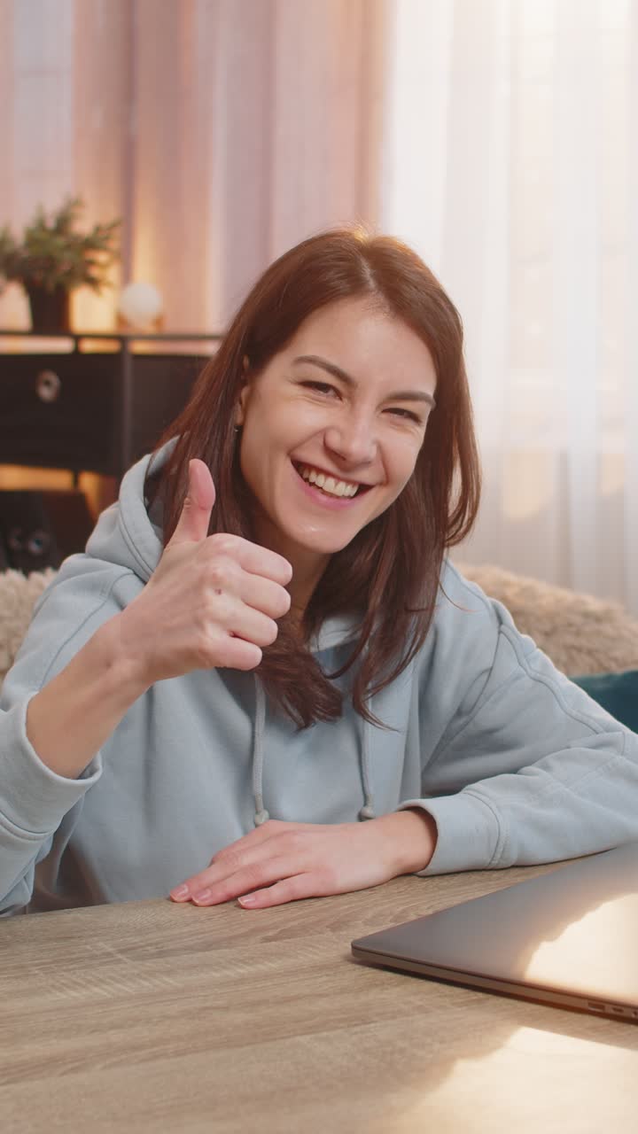 Smiling young woman freelancer closing laptop after work and showing thumbs up at table at home