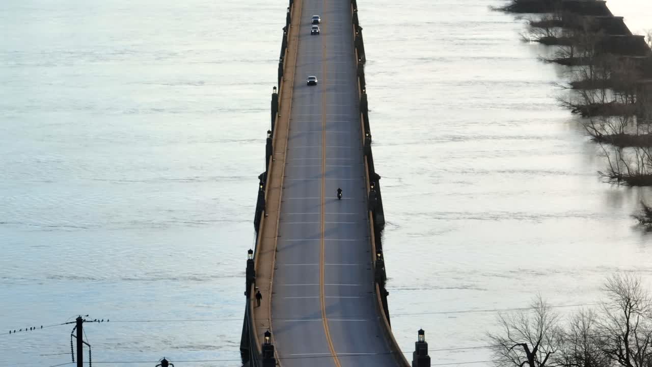 2차선 다리에서 오토바이를 몰고 가는 드론 뷰. 봄에 해가 지는 동안 시내 구역에서 빠져나오는 차량에 접근하고 있다.
