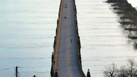 drone view of a motorcycle driving on a two-lane bridge, approaching oncoming vehicles on their way out of a downtown district during sunset in the spring