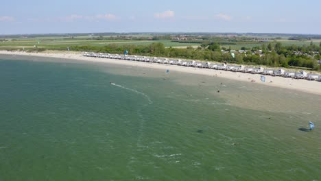 Aerial-orbit-over-the-beach-near-Wissenkerke,-the-Netherlands-on-a-windy-day-with-many-kitesurfers-riding-on-the-wind