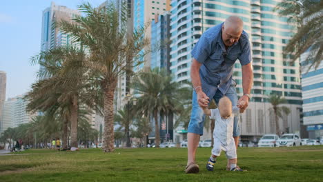 Young-father-with-a-child-and-first-steps.-Young-father-with-a-child-at-outdoor-learninig-for-a-first-steps-near-urban-house-in-the-city