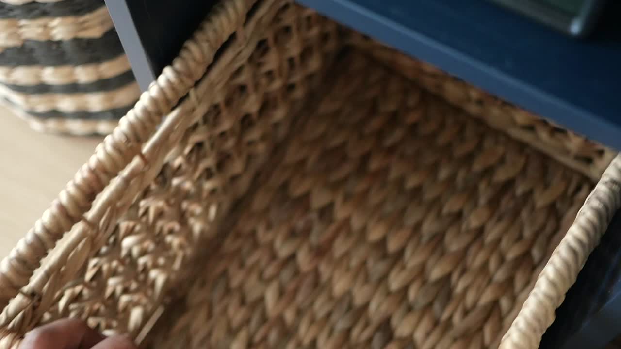 Hand reaching into a wicker storage basket on a dark blue shelf