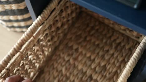 hand reaching into a wicker storage basket on a dark blue shelf