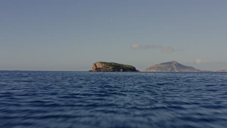 Aerial---Flying-low-over-the-sea-towards-a-small-island-in-Greece