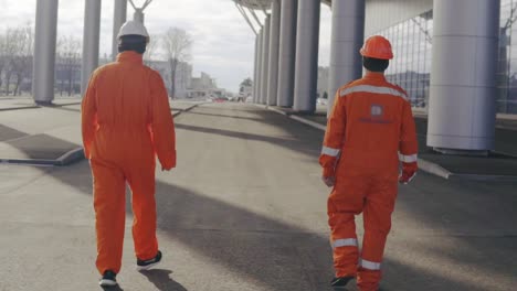 two happy construction workers in orange uniform and helmets walking and jumping together