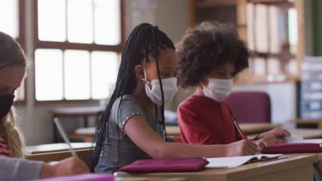 group of kids wearing face masks writing while sitting on their desk at school