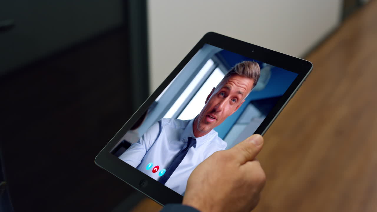 Primo piano di un manager che fa una videochiamata con un tablet mentre cammina nel corridoio di un ufficio. Uomo che negozia con un partner