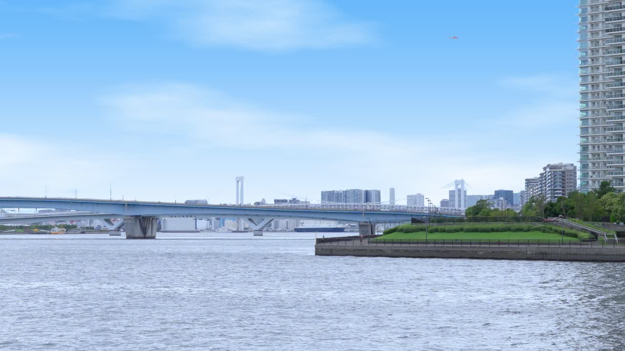 A peaceful shot of a waterfront promenade with a bench, the Harumi Bridge, and the distant Tokyo skyline