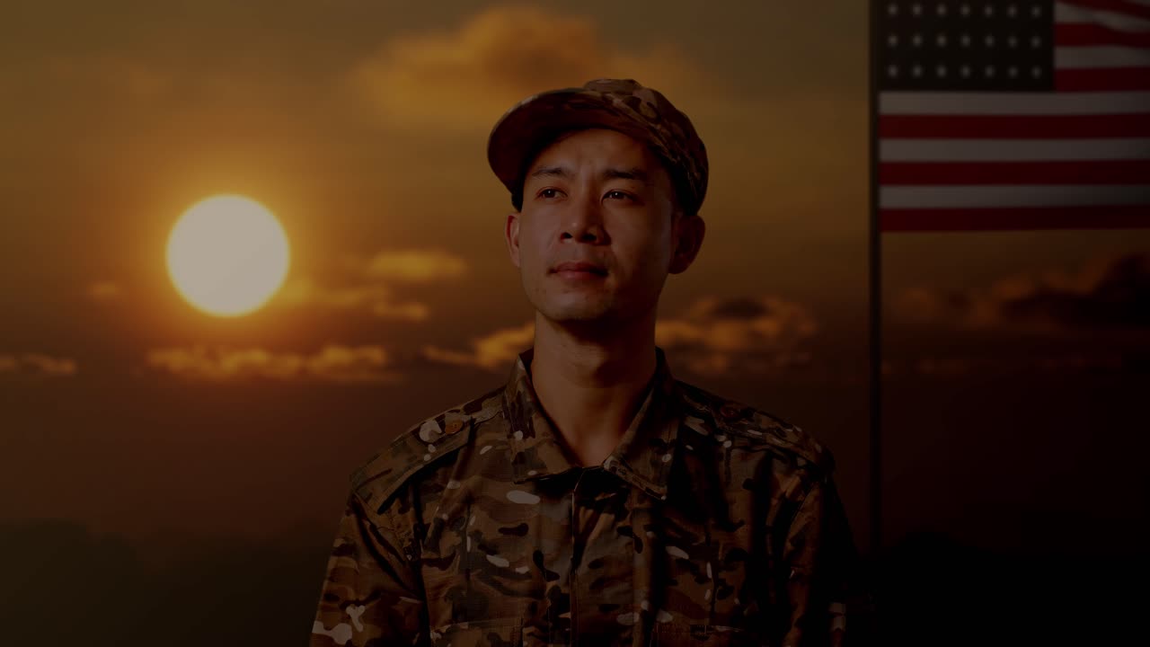 아시안 남성 군인이 미국 발을 들고 서서 주위를 둘러보는 장면, 해가 지는 시간
