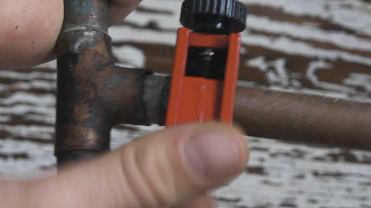 오래된 구리 파이프는 주황색 파이프 커터를 사용하여 남성 손으로 절단됩니다.