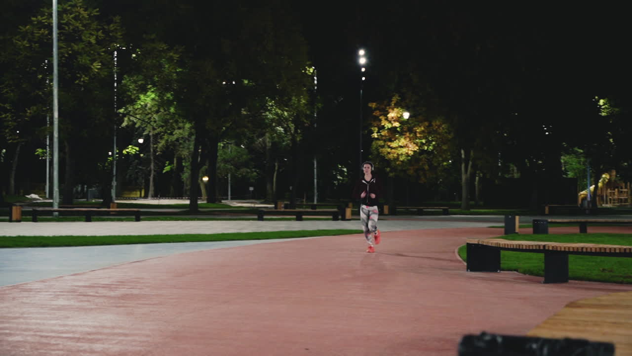 спортивная спортсменка в наушниках bluetooth бежит в парке ночью