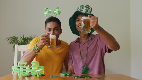 mixed race gay male couple making st patrick's day video call raising glasses wearing costumes