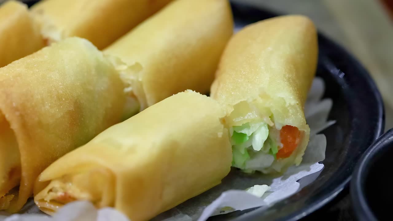 A detailed view of golden-brown spring rolls filled with fresh vegetables, arranged on a black plate.