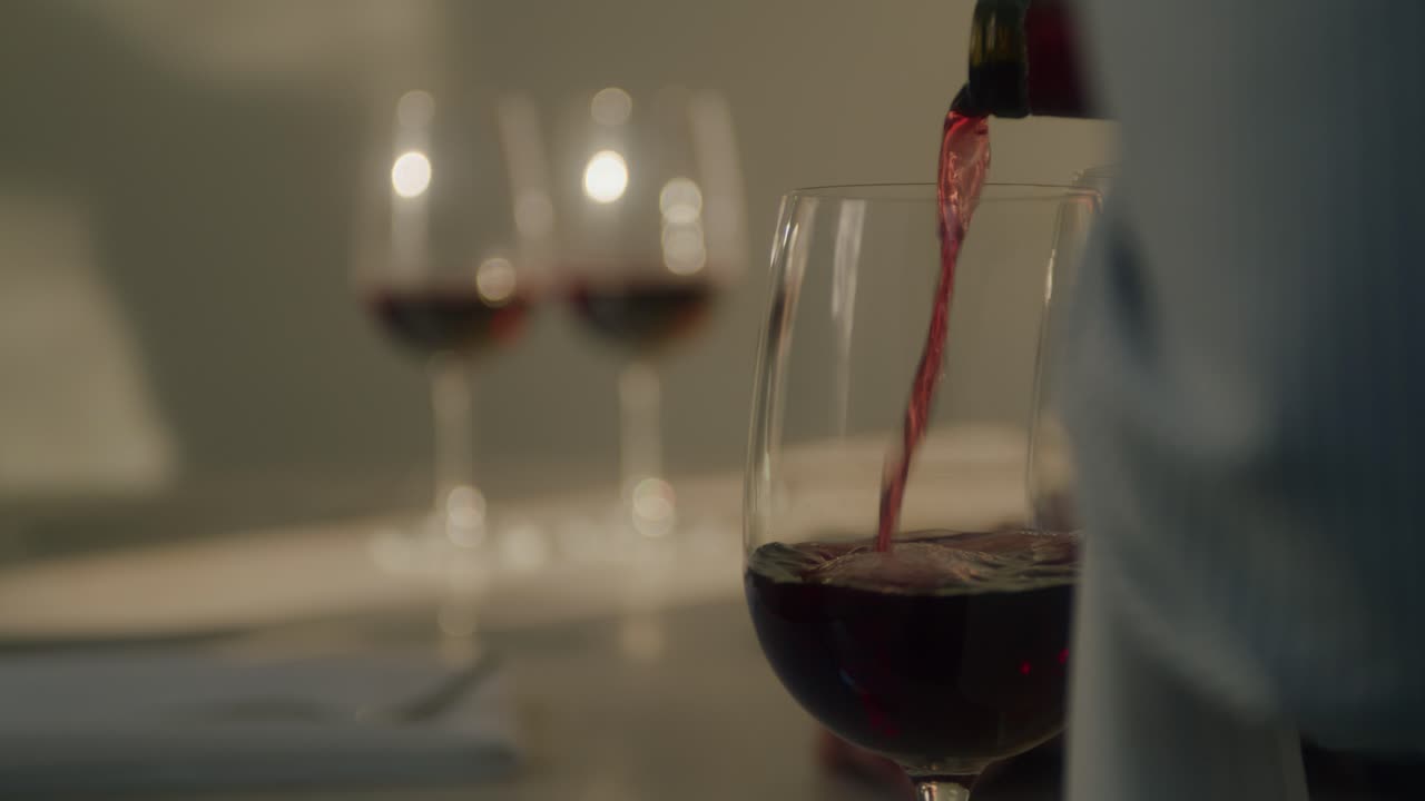 Primo piano di un cameriere che versa bicchieri di vino rosso.