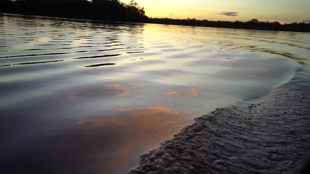 Video POV desde un barco en el río Amazonas en Leticia, Colombia, con un atardecer impresionante, rodeado de aguas tranquilas y árboles silueteados.