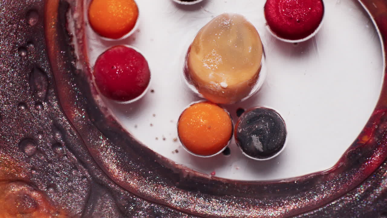 Macro shot of glittery red, orange, black, and brown inks dancing in liquid as a blast of air pushes the pigments into swirling motion