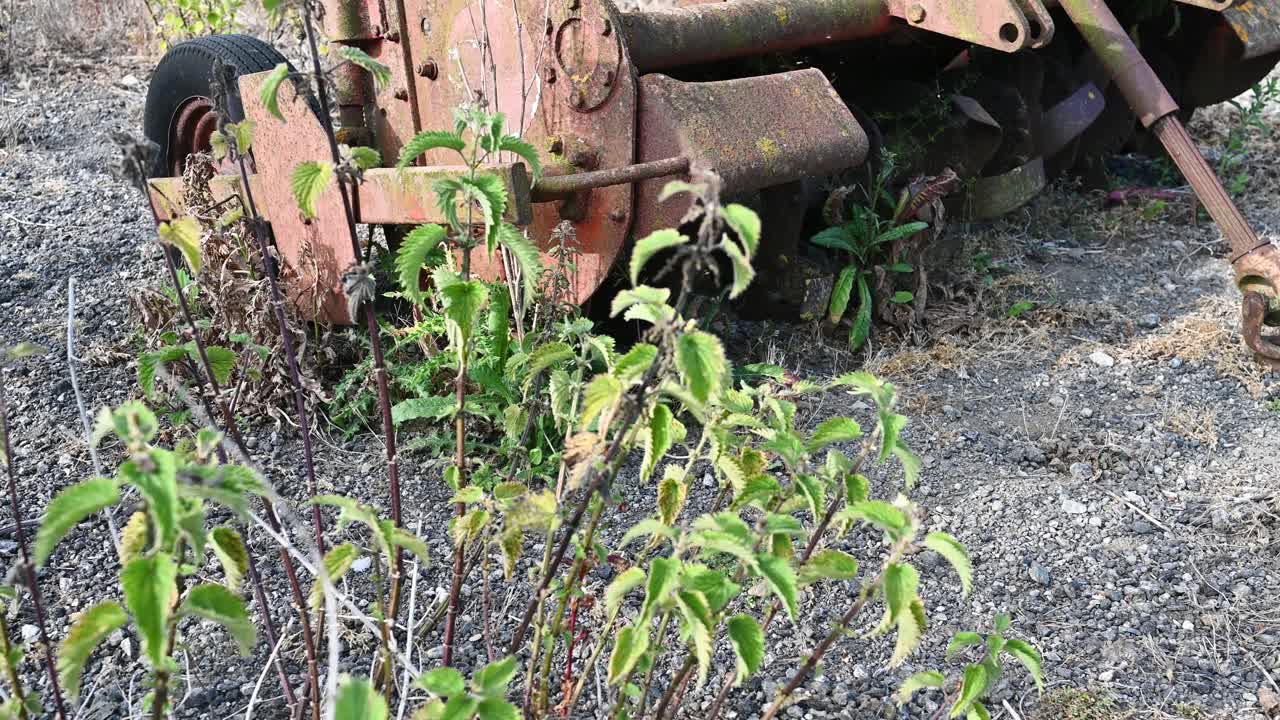 Old farm equipment overgrown and lying abandoned in a farmyard dropping shot ending in nettles