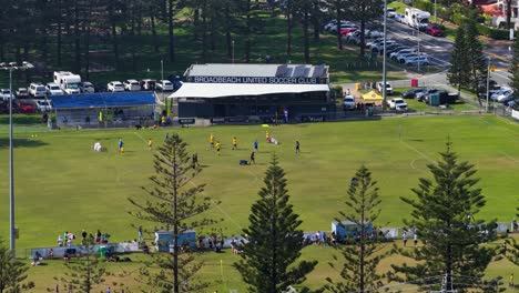 drone footage captures a soccer match at broadbeach, gold coast. sunny day, vibrant colors, and dynamic gameplay