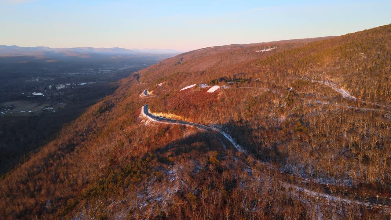 volando sobre una carretera escénica en una montaña alta sobre un vasto valle durante el invierno justo después del atardecer, con un poco de nieve en el suelo