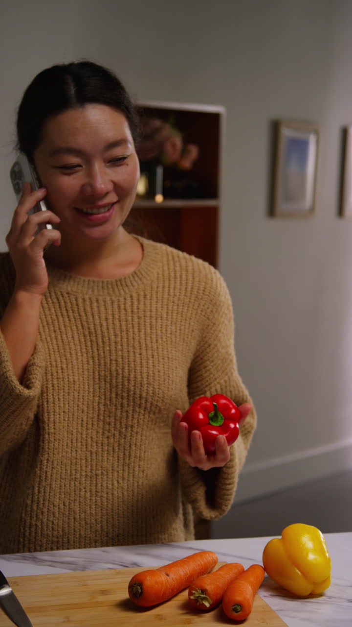 Vertical Video Of Woman Talking On Mobile Phone At Home Preparing Fresh Vegetables For Meal On Counter In Kitchen