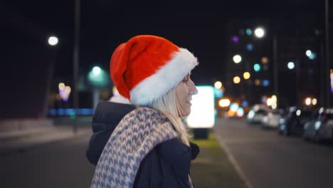 a beautiful woman in a santa claus hat walks at night on christmas