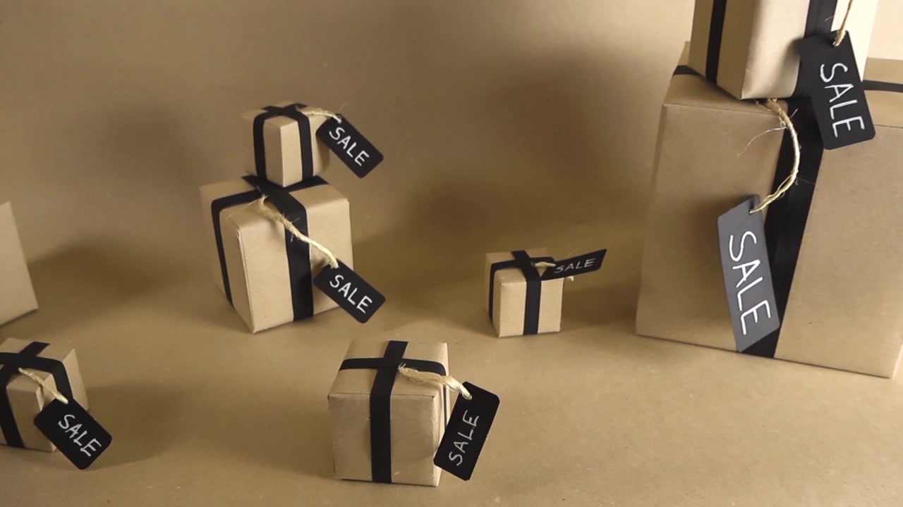 Camera gliding past numerous brown paper gift boxes with black ribbons and sale tags on a neutral background, representing a major shopping event like Black Friday or Cyber Monday sales