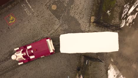 A-pedestal-drone-shot-with-orthomosaic-framing,-capturing-an-empty,-fancy-looking-public-tram-with-a-siren,-exiting-a-closed-area,-in-the-city-of-Sighisoara-on-an-afternoon