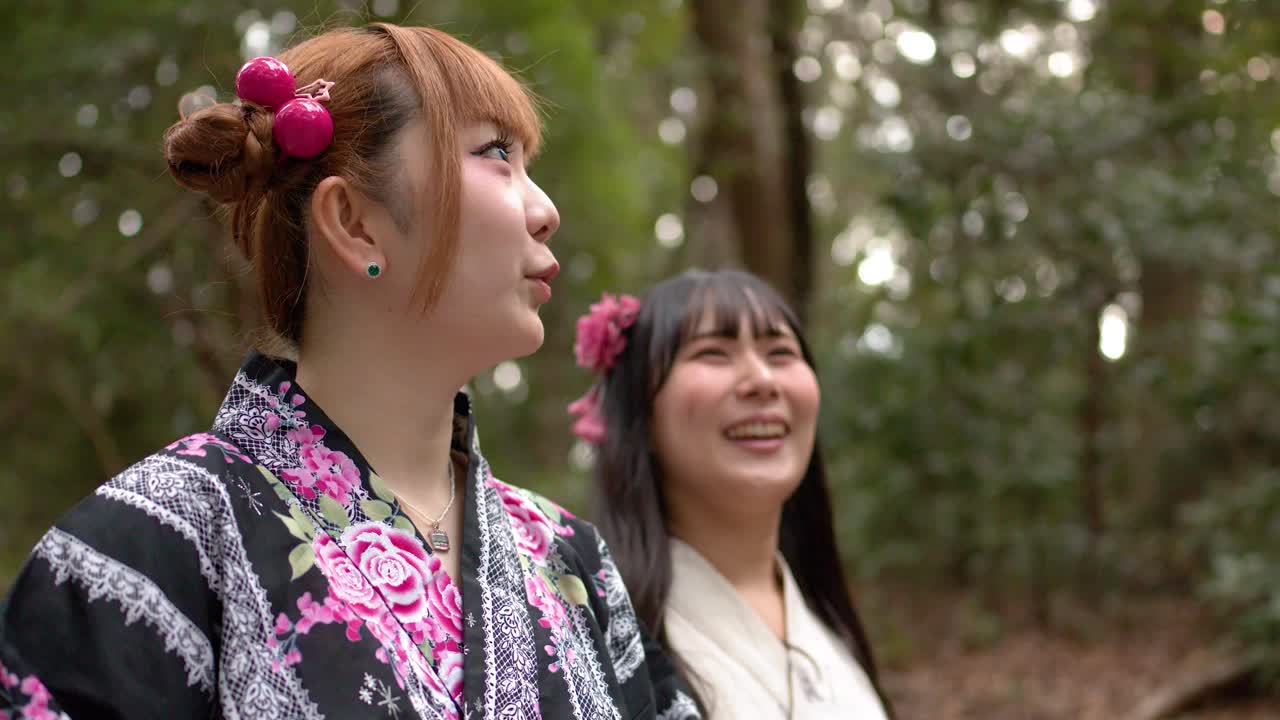 Due donne giapponesi sorridenti che indossano kimono floreali camminano attraverso un lussureggiante parco forestale verde.