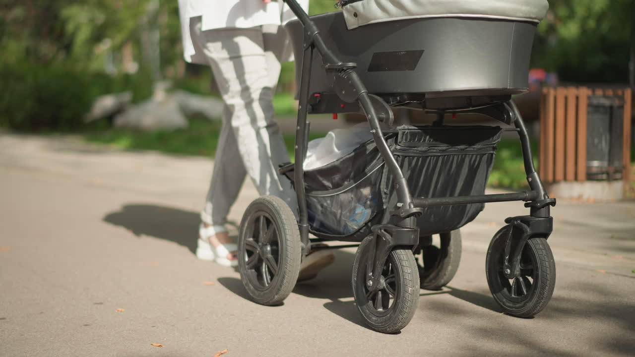 Lågvinkelbild på en vit förälder som skjuter barnvagnshjul längs parkbeläggningen, närbild på robust hjulupphängning som rullar över en solig gångväg, modern barnvagnsdesign visas, produkts mobilitetstest, självsäker.