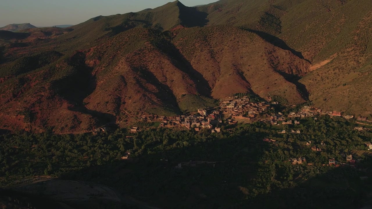 Villaggio di montagna Amazigh che occupa una terrazza fertile nella Valle dell'Ourika, Provincia di Al Haouz, Marrakech-Safi, Marocco, sotto le aspre pendici dell'Alto Atlante, ripresa aerea in movimento