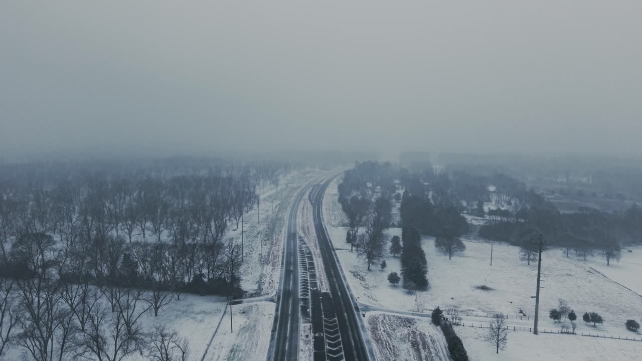 Aerial view of a snow-covered country highway in South Georgia. Rare snowfall blankets the rural landscape. Slow push-in drone movement captures serene winter scenery.