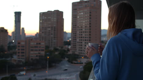 mujer tomando café y mirando la ciudad temprano en la mañana