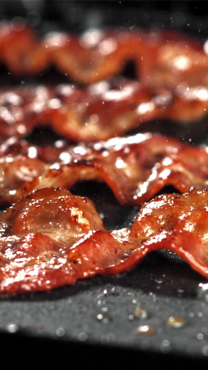 Primo piano di pancetta che frigge e sfrigola in una padella calda