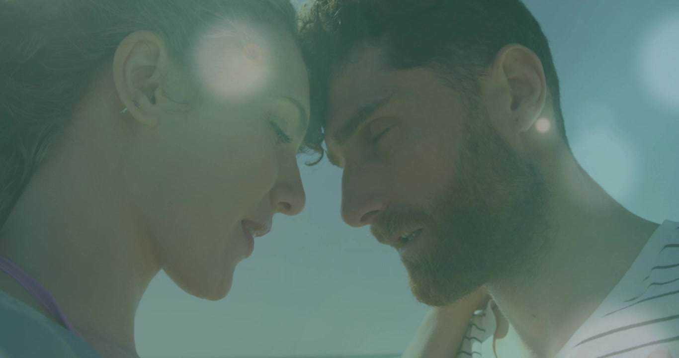 Donna che tocca la spalla dell'uomo, mantenendo lo sguardo, l'uomo che si china, le fronti che si toccano, con un effetto lens flare a scopo di marketing.