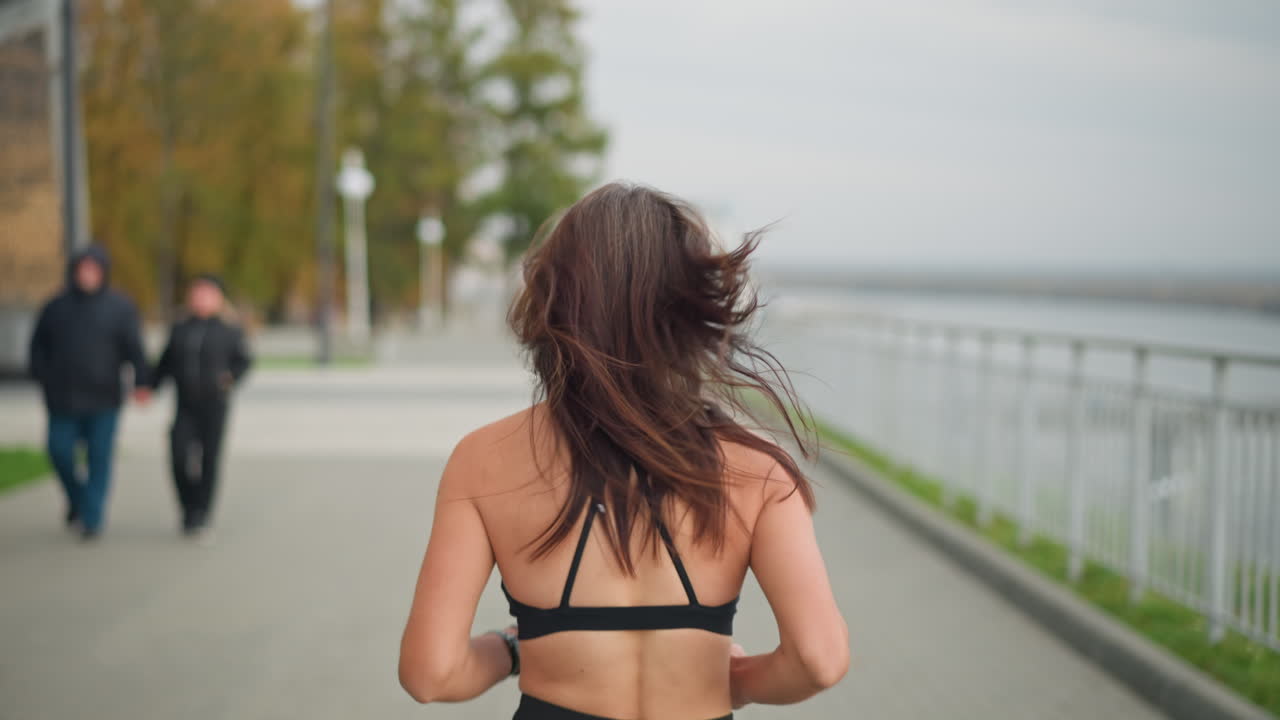 Girl in black neck top jogging past two couples holding hands, blurred background featuring trees, poles, and outdoor park path, showcasing active lifestyle, vitality, and peaceful nature