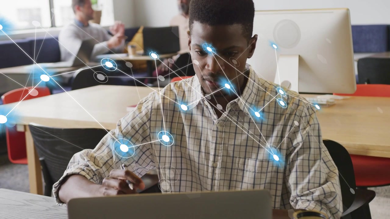 Man writing, opening laptop at desk, causing glowing network overlaying head showing tech data flow