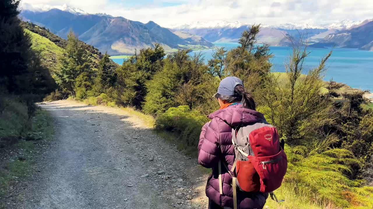 Sporty female hiker on scenic trail in Otago, New Zealand, with lake and mountains view